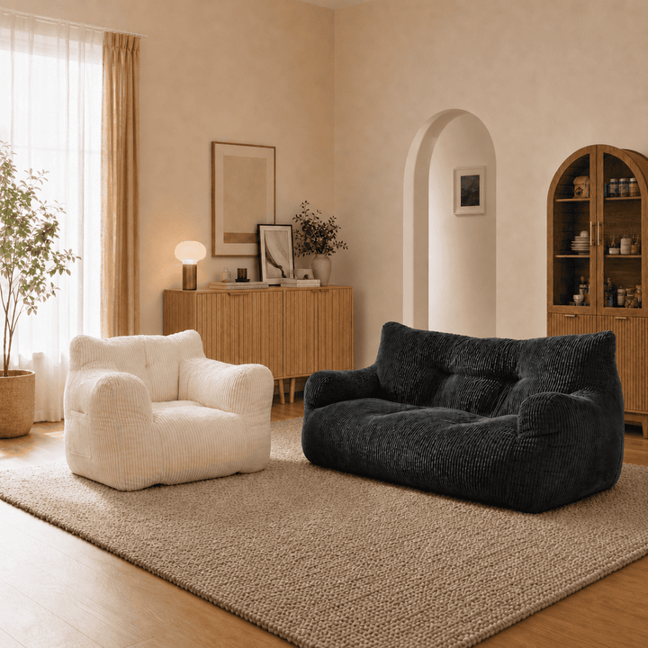 A cozy living room scene with two plush upholstered seating pieces: a white armchair and a black textured sofa, placed on a large beige rug in a warm neutral interior.