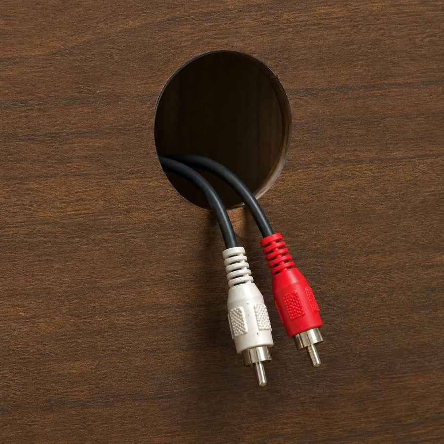 A close-up of a black audio/video cable with white and red RCA connectors emerging from a circular hole in a dark brown wood surface.