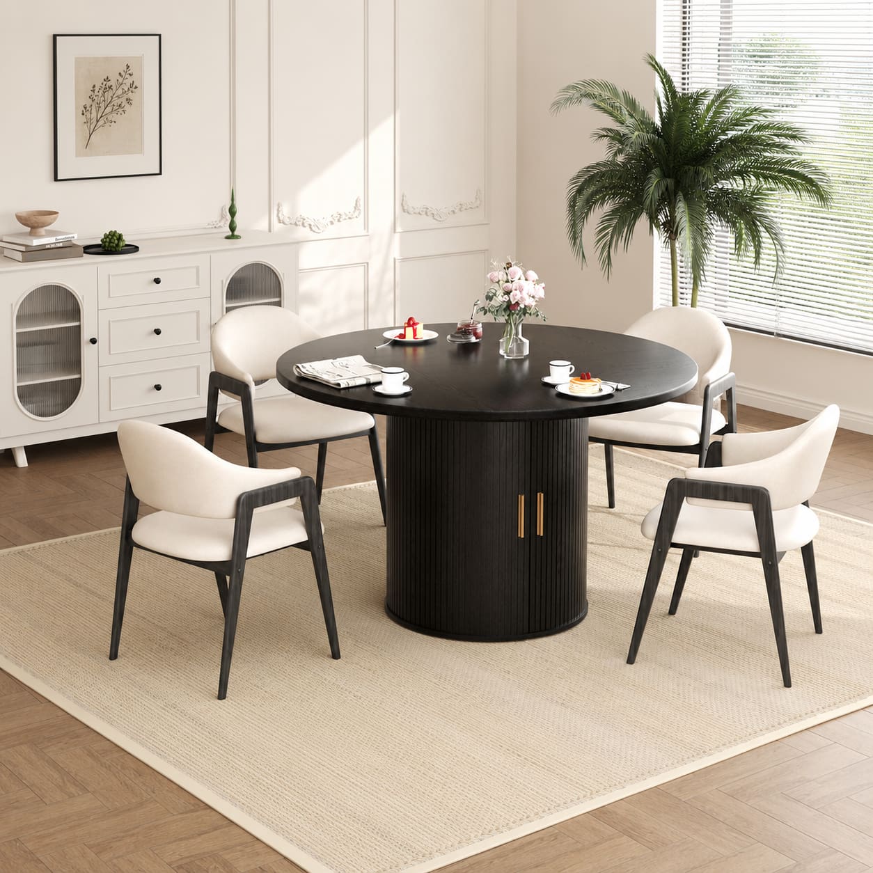 A round black dining table with a ribbed pedestal base and four matching white upholstered chairs with dark legs, arranged on a light rug in a bright, modern dining room.