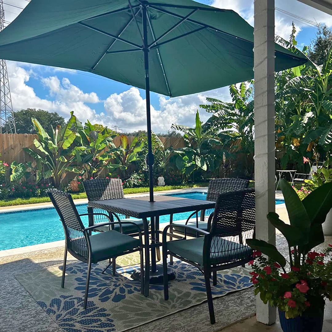 Outdoor patio set with table, chairs, and green umbrella by a poolside.